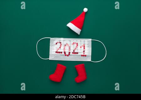 Konzept für Neujahr 2021 und weihnachten. Roter weihnachtsmann Hut und Filzstiefel auf grünem Hintergrund mit medizinischer Schutzmaske aus Coronavirus covid-19 Stockfoto