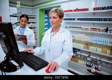 Kaukasischen Apotheker Eingabe auf Desktop-Computer auf der Suche nach Skripten von Patienten stehen in der Apotheke Stockfoto