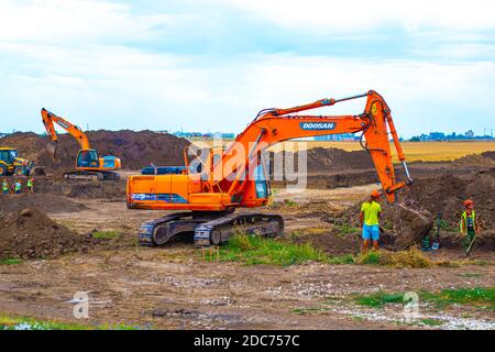 Anapa, Russland-13.07.2020: Bagger gräbt den Boden auf dem Gelände mit Arbeitern. Bau einer Straßenkreuzung Stockfoto