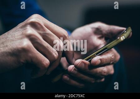 Mann hält und mit einem Smartphone mit beiden Händen. Nahaufnahme, dunkler Ton, unscharfer Hintergrund. Stockfoto