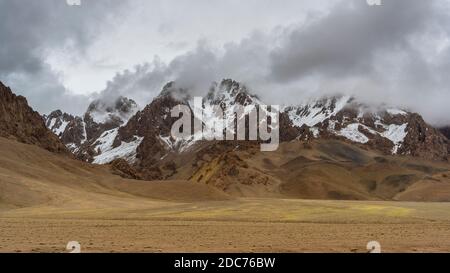 Regen, Wolken und orangefarbene Berge mit Schnee am Pamir Highway in Tadschikistan bei Alichur und Murghab. Stockfoto