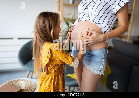 Frohe Familie. Schwangere Mutter und Tochter küssen entspannend zu Hause Stockfoto