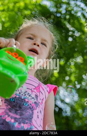 Kleine blonde Mädchen spielt im Park mit Seifenblasen Stockfoto