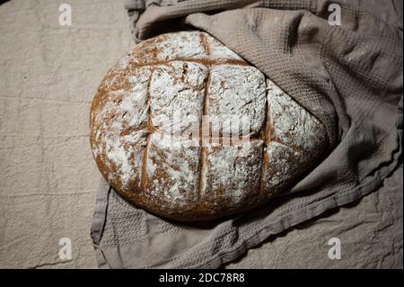 Frisch gebackenes Bauernbrot liegt in einem Tuch gehüllt Kühlen Sie sich auf einer Leinenoberfläche ab Stockfoto