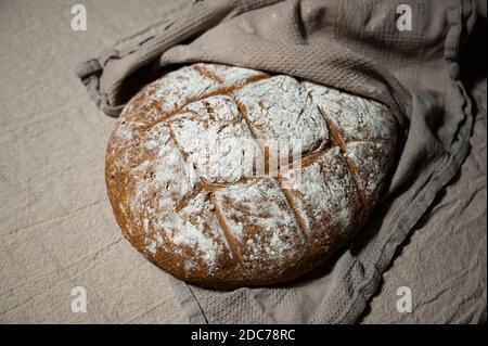 Frisch gebackenes Bauernbrot liegt in einem Tuch gehüllt Kühlen Sie sich auf einer Leinenoberfläche ab Stockfoto
