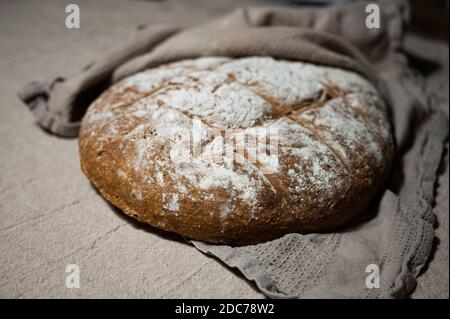 Frisch gebackenes Bauernbrot liegt in einem Tuch gehüllt Kühlen Sie sich auf einer Leinenoberfläche ab Stockfoto