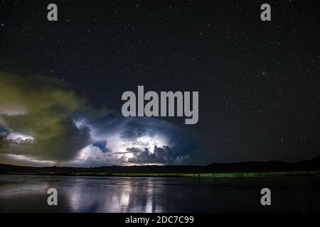 Zahlreiche Blitze beleuchten nachts große Wolken. Sternenklare Nacht am Flussufer vor einem Gewitter. Stockfoto