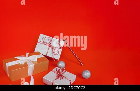 Geschenkboxen, dekorative Glitzerkugeln und Zuckerrohr auf rotem Hintergrund. Weihnachten oder Neujahr Konzept Stockfoto