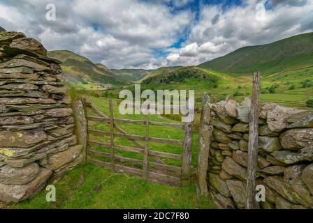 Eine idyllische englische Landszene mit einem zerbrochenen alten Tor mit sechs Bars, das den Blick über grüne Weiden zu fernen Hügeln und malerischen Himmeln führt. Stockfoto