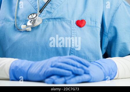 Arzt in blauer Uniform trägt ein Stethoskop und kleine rote Herz Abzeichen Pin, Detail Nahaufnahme, Hausarzt oder Kardiologe im Büro, sitzt am Schreibtisch Stockfoto