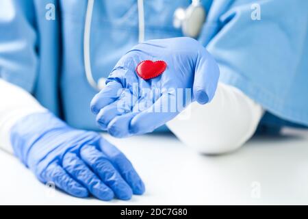 Ärztin mit kleinem roten Herz auf der Handfläche, trägt blaue NHS-Uniform, Detailaufnahme, häufige Gesundheitskontrolle und Prävention Stockfoto