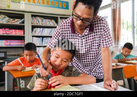 (201119) -- NANNING, 19. November 2020 (Xinhua) -- das Foto vom 19. Juni 2020 zeigt Wei Xuxi, einen Dorflehrer, der die Schreibgesten für einen Schüler in der Shuanggui Grundschule im Bezirk Wuxuan, im südchinesischen Guangxi Zhuang Autonome Region korrigiert. Der 20. November ist der Weltkindertag. Während seiner Kampagne gegen die Armut in den letzten Jahren hat Guangxi die Extrameile gegangen, um Kindern in den von Armut betroffenen Gebieten ein besseres Leben und eine bessere Bildung zu ermöglichen. (Xinhua/Cao Yiming) Stockfoto