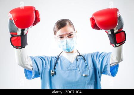 Siegreiche junge kaukasische Ärztin mit blauen Uniform roten Boxhandschuhen, in der Luft erhobene Hände, zufrieden und glücklich nach dem Überleben des Patienten Stockfoto