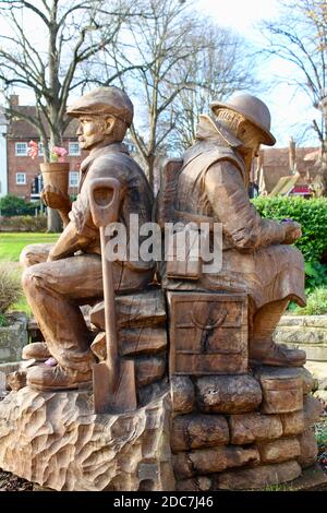 Die Skulptur zeigt zwei Figuren, die als Soldat im Ersten Weltkrieg und später als Kindergärtner dargestellt sind. Die Skulptur ist aus einer Eiche gefertigt. Stockfoto