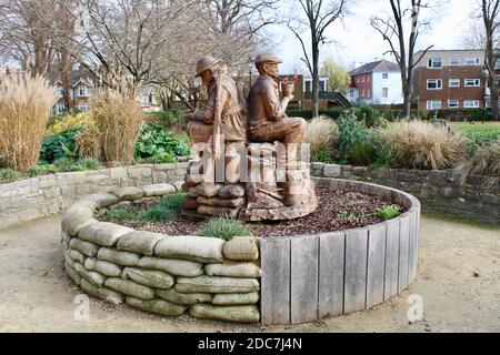 Die Skulptur zeigt zwei Figuren, die als Soldat im Ersten Weltkrieg und später als Kindergärtner dargestellt sind. Die Skulptur ist aus einer Eiche gefertigt. Stockfoto