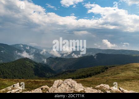 Landschaft von Bergen bedeckt von Wiesen, tiefen Wald und wenige Steine - Valcan Berge in der Nähe Muncel Hügel in Rumänien während des Sommers mit blauem Himmel und Stockfoto