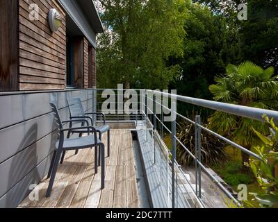 Stühle auf einem Holzbalkon mit Metallschienen in einem modernen Haus mit Blick auf den Garten. Stockfoto