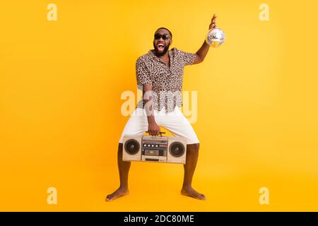 Ganzkörper-Foto von verrückten lustigen dunklen Haut Kerl halten Retro Tape Recorder Glitter Disco Ball Freude Ruhe Party tragen Shorts Leopardenhemd Sonnenbrille Stockfoto