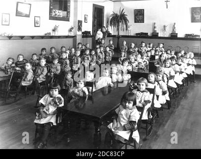 Dies ist ein Klassenzimmer oder Versammlungsraum für jüngere Kinder in einem katholischen Waisenhaus aus dem Jahr 1930 in Milwaukee, Wisconsin, USA. Es sind 58 Kinder hier versammelt, und fast alle haben ein Spielzeug, Puppe, Zugmaschine, Stofftier, Spielzeug Klavier, etc. In diesem Waisenhaus, mit Kindern im Alter von drei bis sechzehn, Mädchen wurden die häusliche Kunst gelehrt, und Jungen gelernt Malerei, Tischlerei, Handwerk und Holzschnitzerei. Die älteren Kinder hatten auch eine 30-köpfige Band, die für lokale Bürgerveranstaltungen spielte. Um meine Kinder-bezogenen Vintage-Bilder zu sehen, Suche: Prestor vintage Kids Stockfoto