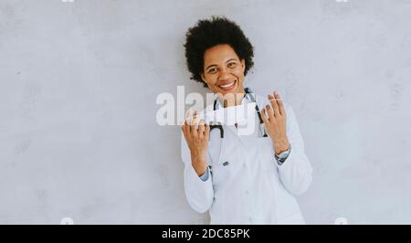 Weibliche afroamerikanische Arzt tragen weiße Uniform und Abheben Gesichtsmaske im Krankenhaus Stockfoto