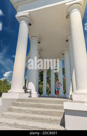 Frau besuchen Kolonnade in Tschernomorsk Stadt an einem sonnigen Sommertag, Ukraine. Schwarzes Meer im Hintergrund. Stockfoto