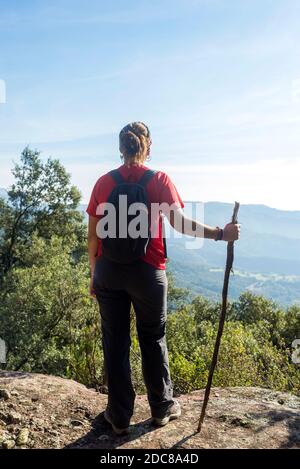 Rückansicht einer jungen Frau, die auf einem hohen Berg steht Halten Sie einen Stock Stockfoto