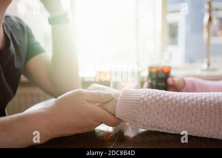 Anonymes romantisches Paar, das Hände hält, während es am Tisch mit sitzt Getränke im Café Stockfoto