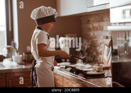 Ein kleiner Junge kocht Pfannkuchen in der Küche Stockfoto