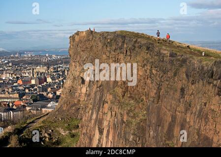 Läufer und Hundewanderer genießen die November-Sonne auf den Salisbury Crags, Edinburgh, Schottland, Großbritannien. Stockfoto