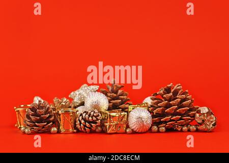 Weihnachtsarrangement mit goldenen Baumkugeln, Geschenkschachteln und Tannenzapfen auf hellrotem Hintergrund mit leerem Kopierraum Stockfoto