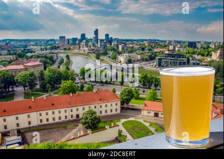 Glas Bier mit Blick von oben auf Vilnius, Litauen. Blick auf Vilnius, rote Dächer, Fluss, Wolkenkratzer im Geschäftsviertel. Stockfoto