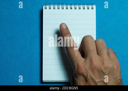 Mann Hand Punkte auf weißem Notizbuch. Hellblauer Hintergrund Stockfoto