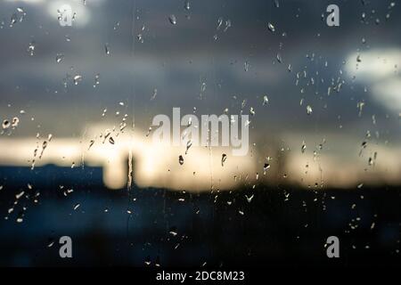 Aindrops auf dem Glas eines Fensters, verschwommener Wolkenhimmel im Hintergrund. Selektiver Fokus. Stockfoto