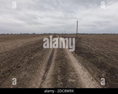 Stromleitungen entlang einer unbefestigten Straße. Düstere Abendlandschaft. Stockfoto