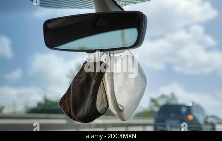 Zwei Schutzmaske hängen von te Rückspiegel eines Autos. Selektiver Fokus. Verschwommener Hintergrund. Stockfoto