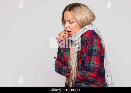 Verärgert junge Frau in kariertem Hemd, in Schal gehüllt Husten, geschlossenen Augen. Kranke Frau hat Grippe-Symptom. Krankheitskonzept. Stockfoto