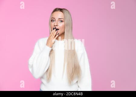 Überrascht junge Frau mit langen blonden Haaren bedeckt Mund mit der Hand und Blick auf die Kamera, isoliert auf Studio rosa Hintergrund. Stockfoto