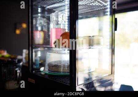 Verschwommenes Bild von Showcase im Café-Shop. Kuchen und Krug mit Getränk auf den Regalen eines Fensters eines Straßenrestaurants Stockfoto