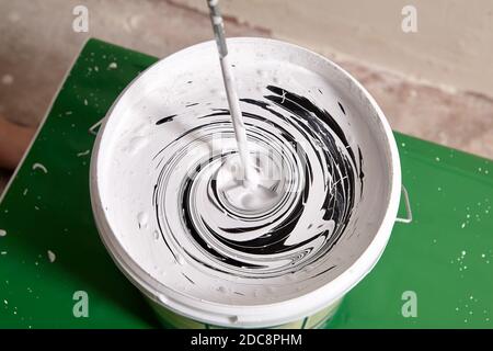 Mischen von Farben im Korb mit Hilfe von Bohrer. Handwerker macht neue Farbe mit Arbeitswerkzeug während der Renovierung. Stockfoto