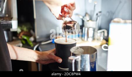 Der Barista gießt Espresso in die Einweg-Papiertasse. Zubereitung von leckeren Kaffee trinken mit Milch. Verschwommenes Bild, selektiver Fokus Stockfoto