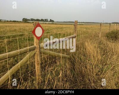 schild an der Säule mit Stacheldraht, Gitter mit Stacheldraht, wolkiger Himmel, trockenes Feldgras, eingezäuntes Territorium, Warnung, Aufmerksamkeit Stockfoto