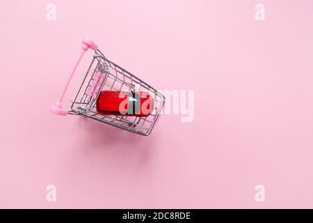 Rotes Spielzeugauto in einem Einkaufswagen auf einem pastellrosa Hintergrund, Draufsicht, Kopierraum. Das Konzept der Kauf eines Autos online, ein Geschenk für Valentinstag, wome Stockfoto