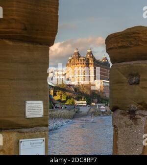 Ein Blick auf das sonnendurchflutete Grand Hotel, Scarborough von zwischen zwei Säulen. Eine Promenade führt zu den Gebäuden und das Meer ist im Vordergrund. Stockfoto