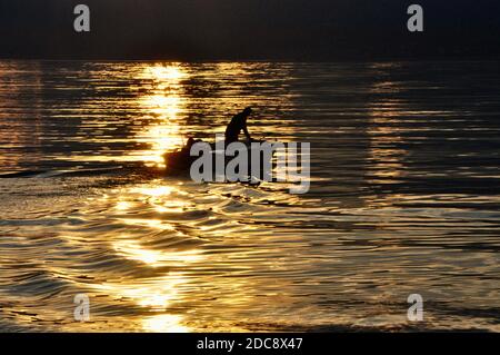 Boot und Fischer in wunderschönen Sonnenuntergang an der Adria Kroatien-Kvarner. Kleines Fischerboot auf goldenem Meer, Wellen. Fischerboot unter der Mitternachtssonne. Stockfoto