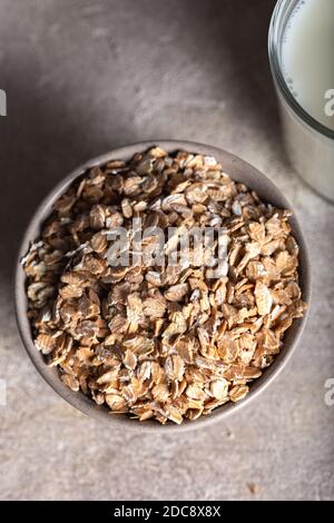 Roggenflocken in einer Schüssel mit einem Glas Milch auf einem Steingrund. Gesunde Getreideflocken in einer Keramikschale und Milch aus nächster Nähe. Stockfoto