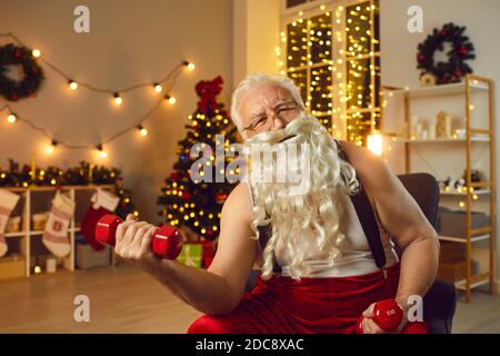 Happy Santa Claus sitzt im Sessel in seinem Wohnzimmer und Training mit Kurzhanteln Stockfoto