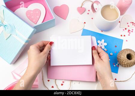Ein Umschlag und ein weißes leeres Blatt in den Händen einer Frau auf einem romantischen Hintergrund in rosa Tönen. Stockfoto