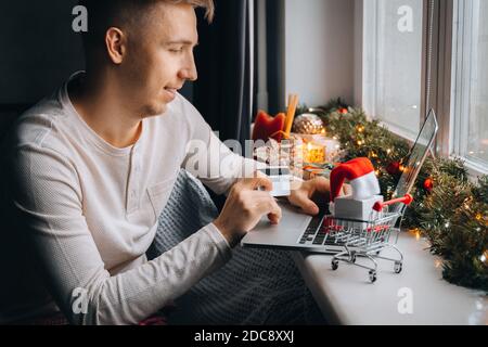 Mann Kunde hält Kreditkarte Online-Shopping Zahlung im Internet-Shop zu Hause. Weihnachten Geschenk-Box Dekoration, Neujahr Winter Verkauf, Weihnachten d Stockfoto