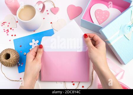 Eine Frau zieht einen Brief aus einem rosa Umschlag auf einem romantischen Hintergrund mit Herzen. Stockfoto