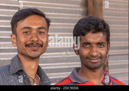 Chikkanayakanahalli, Karnataka, Indien - 3. November 2013: Nahaufnahme Porträt von 2 jungen lächelnden Männern. Wellpappen aus Metall als Hintergrund. Zusätzliche Kleidungsstücke Stockfoto